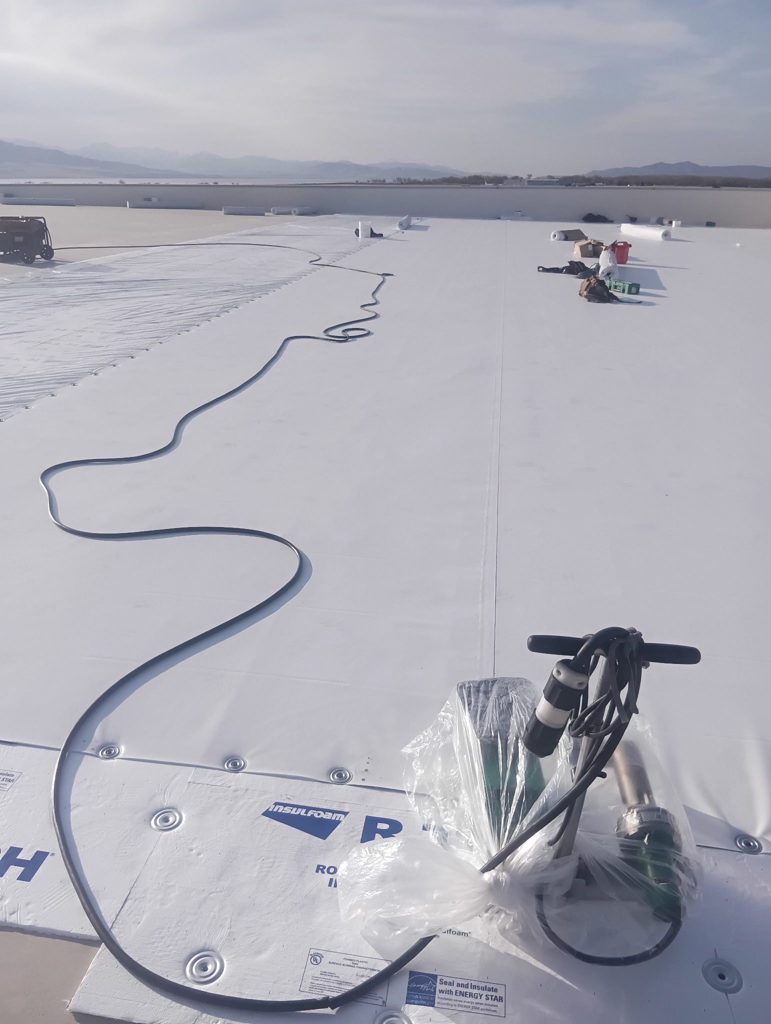 Flat commercial roof installation with insulation and roofing equipment under clear skies.