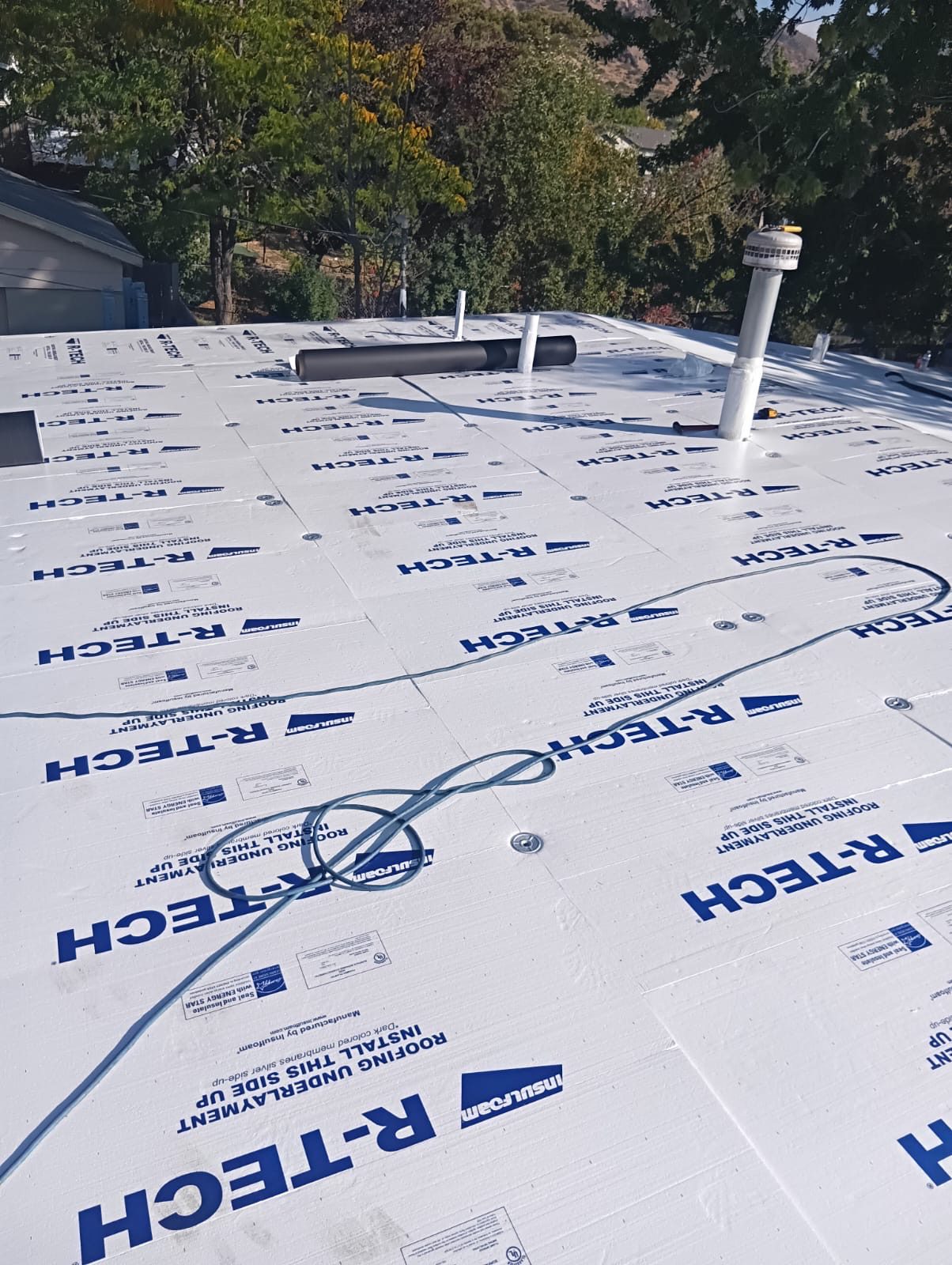 Rooftop installation with insulation boards, vent pipe, and blue hose—demonstrating energy-efficient roofing and insulation system.