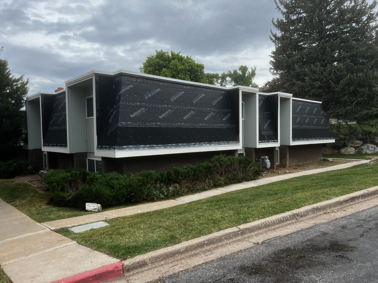 Commercial building under renovation with black construction wrap and flat roof, surrounded by landscaping and sidewalk.